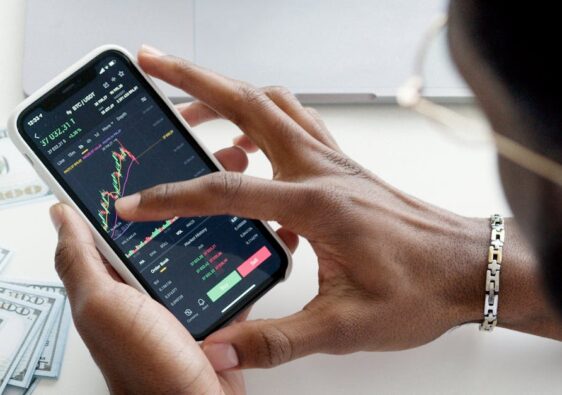 A person trading stocks using a smartphone, showcasing financial data on mobile and laptop screens.